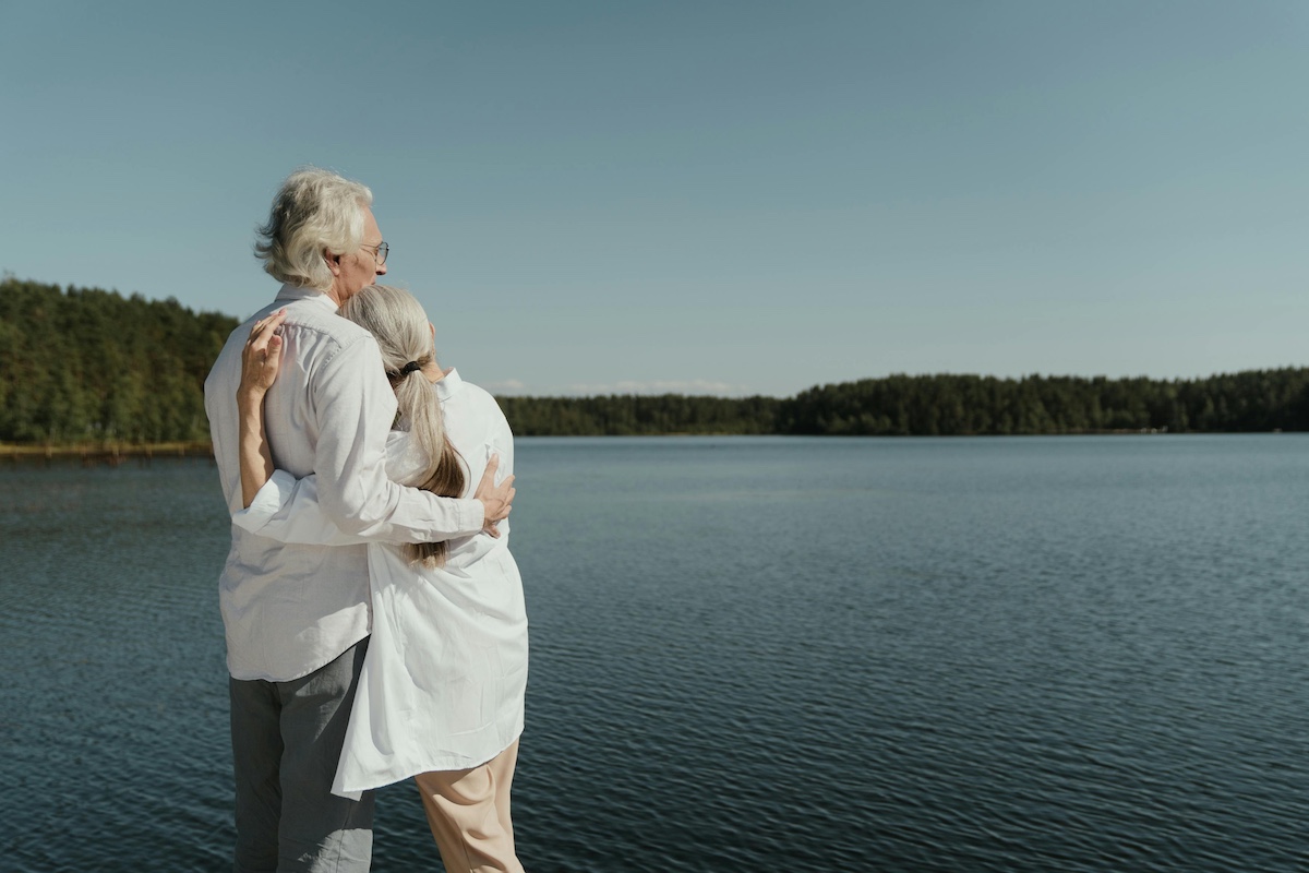 Older couple embracing while overlooking a pristine lake.