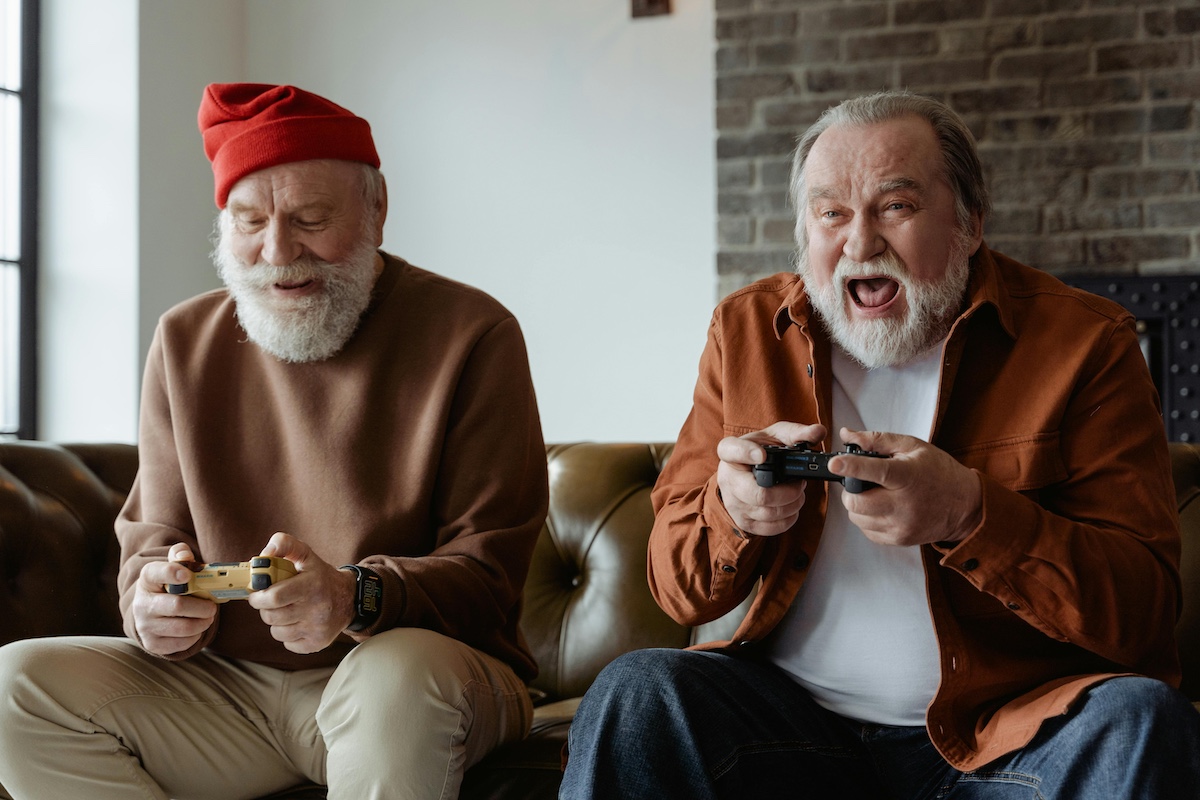 Two older men sitting on sofa and playing video games.
